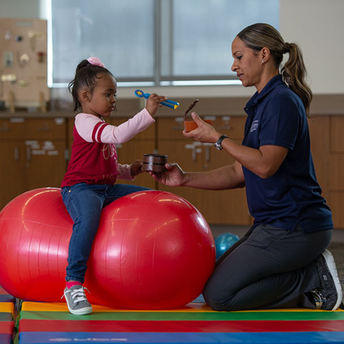 occupational therapy assistant working with child to pick up objects using tongs